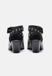 Zwarte hakken met een open achterkant, voorzien van een cross-strap ontwerp accentueert met zilveren grommets. Gemaakt van glad leer met een stevige blokhak.