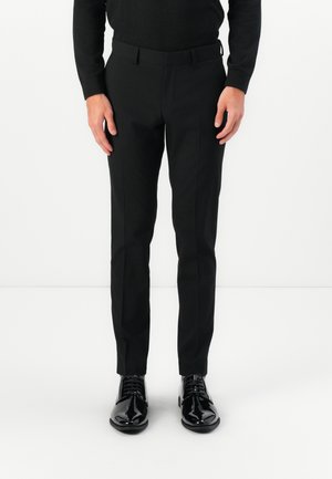 Pantalones negros, ajustados y de corte recto con un suave pliegue, hechos de una tela suave. Combinados con elegantes zapatos de vestir negros.