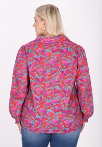 Farverig bluse med et blomster mønster i pink, rød og blå. Har puffede ærmer og en krave, lavet af et let stof.