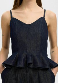 Denim peplum top s tenkými ramínky, tmavě modré barvy, strukturovaným tělem a rozšířeným lemem. Obsahuje viditelné švy a texturovaný povrch.