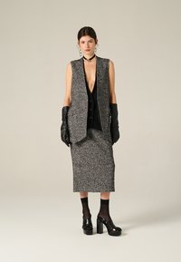 Gilet grigio testurizzato sopra una maglietta nera, abbinato a una gonna grigia coordinata. Guanti in pelle nera e tacchi a piattaforma completano l'outfit.