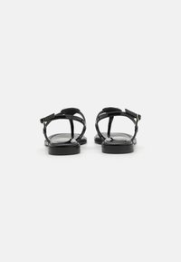 Plat zwarte gelakte leren sandalen met dunne bandjes en een verstelbare enkelgesp, met een gladde textuur en minimalistisch ontwerp.