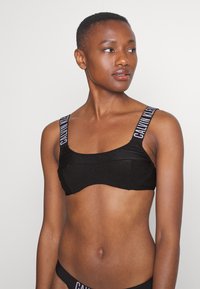 Črn rebrast bralet iz teksturirane tkanine, z širokimi naramnicami z logotipom 'CALVIN KLEIN'. Kvadratni dekolte in prilegajoč oblikovanje.