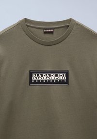 T-shirt in cotone verde oliva con logo rettangolare nero e testo bianco. Collo rotondo e maniche corte. Texture liscia.