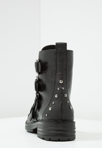 Černá kožená kotníková bota s texturovaným povrchem, třemi dekorativními sponami a kovovými hřebíky na zadní straně, vybavená pevnou gumovou podrážkou.