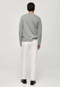 Grauer Strickpullover, weiße Hose, schwarze Schuhe. Der Pullover hat einen runden Ausschnitt und lange Ärmel. Die Hose hat einen geraden Schnitt.