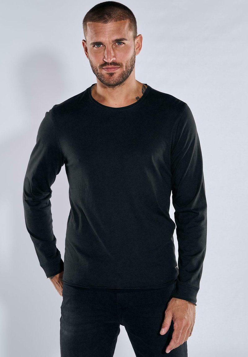 Schwarzes Langarmshirt mit rundem Ausschnitt, weichem Material und taillierter Passform. Kombiniert mit dunklen Jeans für einen stimmigen Look.