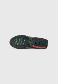 Nike shoe sole featuring black rubber with textured grip patterns, green accents, and red circular details. Prominent flex grooves for flexibility.