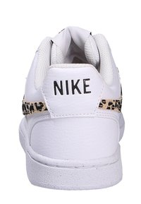 White leather sneaker with a textured finish, featuring a leopard print accent and black Nike logo on the heel. Flat rubber sole.