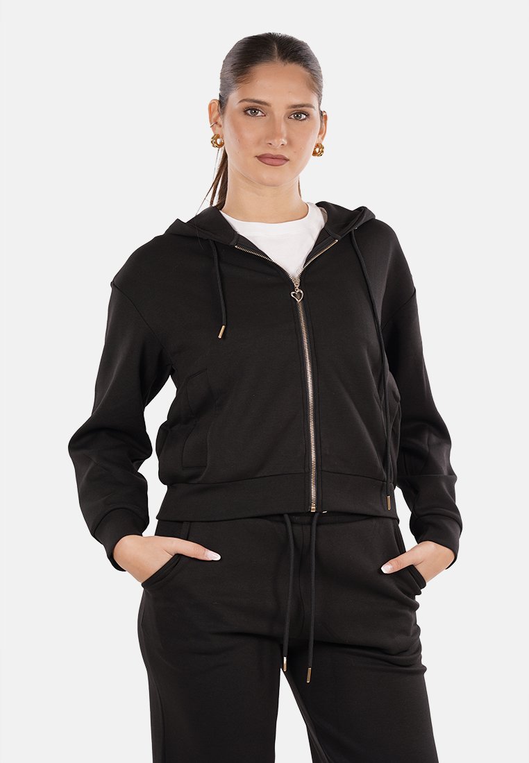 Felpa corta nera con zip realizzata in tessuto morbido, caratterizzata da un cappuccio, tasche frontali e dettagli dorati sulla zip e sui lacci.