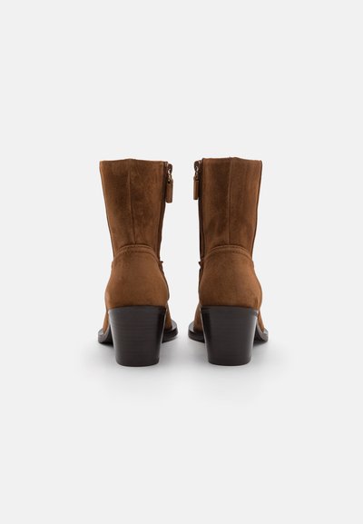 Bottes de cheville en suède marron avec un bout arrondi, un talon empilé et une fermeture éclair à l'arrière. Présente des détails de couture le long des coutures.
