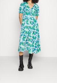 Blommig midiklänning med V-ringning och korta puffärmar. Har gröna och blå abstrakta mönster på lätt tyg. Matchad med svarta stövlar.