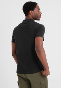 Black polo shirt with short sleeves. Ribbed collar and cuffs. Smooth cotton fabric, fitted design. Worn with olive green cargo pants.