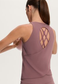 Sleeveless workout top in muted mauve, featuring a crisscross back design, smooth texture, and a curved hem with a side pocket.