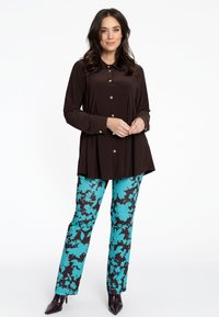 Braune Knopfbluse mit Kragen, kombiniert mit türkisfarbene und schwarzen Blütenmuster-Hosen. Die Hose hat einen geraden Schnitt und eine glatte Textur.