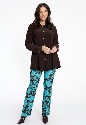 Braune Knopfbluse mit Kragen, kombiniert mit türkisfarbene und schwarzen Blütenmuster-Hosen. Die Hose hat einen geraden Schnitt und eine glatte Textur.