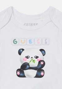 White baby onesie featuring a cartoon panda holding bamboo. The design includes colorful block letters spelling "GUESS" above the panda.