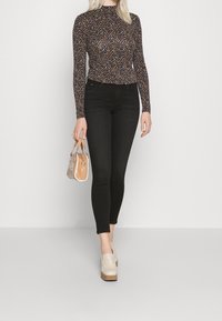 Top ajustado de manga larga con un patrón de lunares multicolores, combinado con unos pantalones ajustados negros de tiro alto y zapatos de plataforma beige, sosteniendo un bolso pequeño.