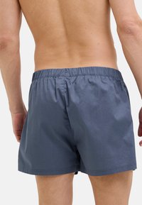 Miestne tmavosivé plavky s elastickým pásom, vyrobené z ľahkej tkaniny. Majú jednoduchú, hladkú textúru a žiadne viditeľné vzory.