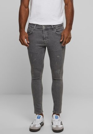 Jeans grises ajustados con parches deslavados, bolsillos frontales y cierre de botón metálico, combinados con zapatillas blancas con acentos azules y negros.