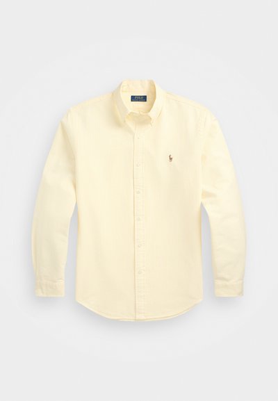 Camisa amarela de manga longa com botões, com riscas verticais subtis, hem arredondado e um pequeno logótipo bordado no lado esquerdo do peito.