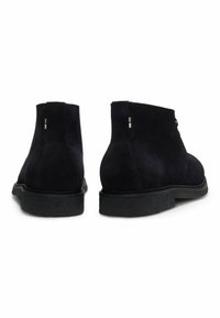 Stivali alla caviglia in suede nero con suola in gomma testurizzata, caratterizzati da hardware decorativo minimale sul tacco e un'allacciatura frontale.