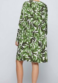 Robe à motifs de feuilles vertes avec manches longues, coupe décontractée et dos légèrement froncé. Fabriquée dans un tissu léger à texture lisse.