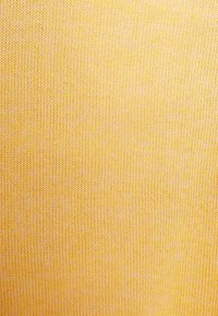 Detailní záběr na žlutou pletenou tkaninu, který ukazuje složitý vzor a strukturu propletené příze.