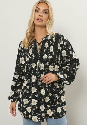 Schwarze Bluse mit beigem Blumenmuster, gerafftem Rundhalsausschnitt mit Bändern, langen Puffärmlen und strukturierten Details im Oberteil. Leichter Stoff.