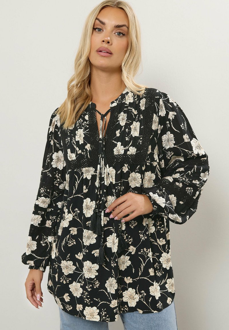 Blusa nera con motivo floreale beige, scollatura arricciata con lacci, maniche lunghe a sbuffo e dettagli in tessuto sulla parte superiore. Tessuto leggero.