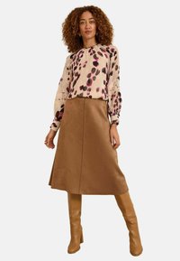 Viegls, garām piedurknēm blouse ar rozā un melnu leopardu druku, apvienota ar brūnu, līdz ceļiem garu svārku un bēšām līdz ceļiem garām zābakiem.
