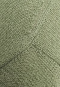 Zielona dzianina o teksturowanej powierzchni, z ukośnym wzorem i miękkimi, puszystymi włóknami. Jednolity odcień bez widocznych elementów metalowych.