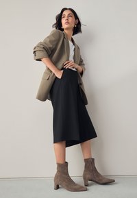 Blazer beige, camicia bianca, gonna midi nera e stivaletti taupe in camoscio. Linee pulite e vestibilità rilassata con dettaglio zip sugli stivaletti.