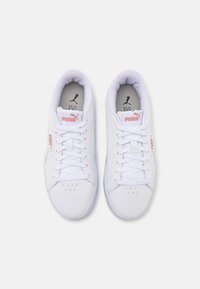 White sneakers with a smooth leather upper, lace-up design, and pink logo accents. Features round toe and perforated detailing on the toe box.