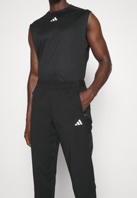 Svart ärmlös atletisk topp med en vit logotyp och matchande svarta byxor med en vit logotyp. Materialet verkar lätt och slätt.