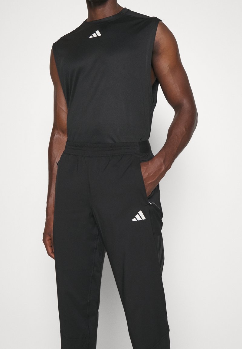 Svart ärmlös atletisk topp med en vit logotyp och matchande svarta byxor med en vit logotyp. Materialet verkar lätt och slätt.