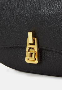 Sac en cuir noir avec surface texturée et détail de fermeture en métal doré. Sa forme est arrondie avec de subtils accents de couture.