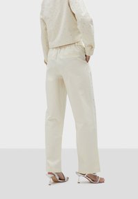 Crème-kleurige katoenen blouse met versieringen, gecombineerd met lichte crèmekleurige broek met zakken en een subtiele logo-accent.