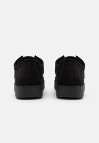 Chaussures en daim noir à finition texturée, dotées d'une semelle en caoutchouc noire à profil bas et d'un design arrière arrondi. Aucun élément métallique ou accent visible.