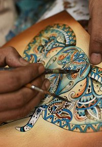 Handmatig een ingewikkeld blauw en oranje gepatroond olifant schilderen op gestructureerd papier. Twee kwasten vastgehouden in de handen, gefocust op de details.