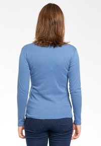 Maglia a maniche lunghe di colore blu in cotone morbido, design aderente, texture liscia, orlo curvato, indossata con jeans scuri, vista da dietro.