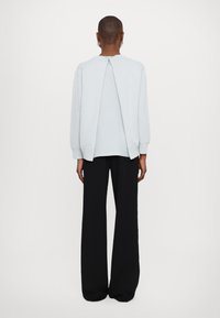 Ljusgrå sweatshirt med öppning bak och dragkedjeddetalj, långa ärmar och avslappnad passform, i kombination med vida svarta byxor.