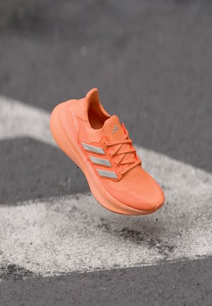 Bright orange athletic shoe with a textured upper, reflective silver stripes, and a cushioned sole, suspended above a gray surface.