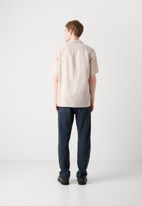 Short-sleeve, light beige shirt with a relaxed fit and a fold-down collar, paired with dark blue denim jeans and black shoes.