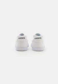 Hvite Lacoste-sneakers med overdel i lerret, polstret krage, flate lisser og gummisåle. Har merkevarelogo på hælen og baksiden.