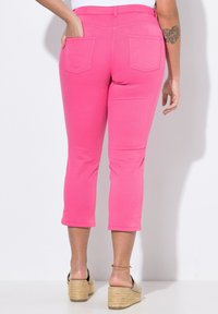 Růžové zkrácené kalhoty s hladkým povrchem, které mají dvě zadní kapsy a přiléhavý střih. Nosí se s espadrilkami světlé barvy.