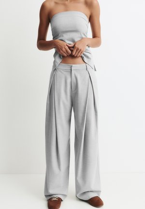 Grijze strapless top gecombineerd met loszittende grijze geplooide broek. De stof lijkt glad, de broek heeft zakken en een wijd been ontwerp.