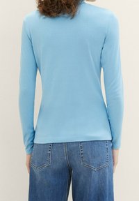 Helles blaues Langarmoberteil, weicher Stoff, taillierte Passform, runder Ausschnitt, glatte Textur, kombiniert mit hochgeschnittenen blauen Jeans mit Taschen.