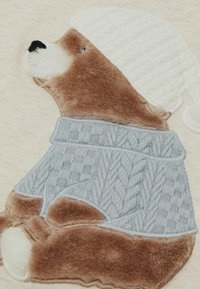 Oso de peluche marrón que lleva un suéter de punto azul claro con un patrón texturizado y un gorro de punto blanco. La textura suave y peluda es prominente.
