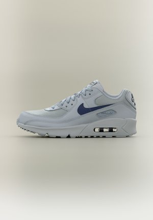 Lys grå Nike Air Max-sneaker med marineblå Swoosh, mesh- og skinnøvre, synlig luftpute i sålen, på nøytral bakgrunn.